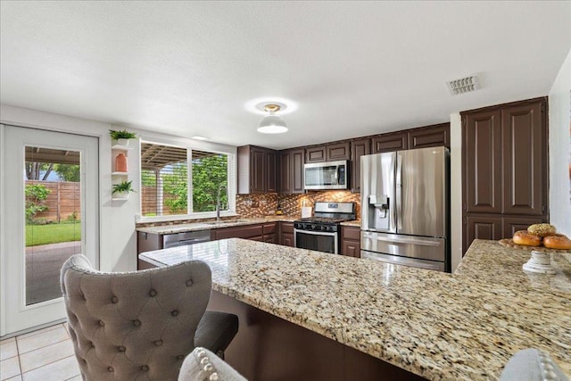 8204 Seminary Ridge Dr, Austin, TX 78745 - kitchen featuring appliances with stainless steel finishes, a peninsula, backsplash, light stone counters, and a kitchen breakfast bar