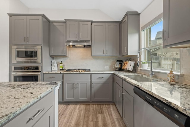 608 Roaming Dr, Hutto, TX 78634 - kitchen with gray cabinetry, appliances with stainless steel finishes, light wood-style floors, tasteful backsplash, and under cabinet range hood