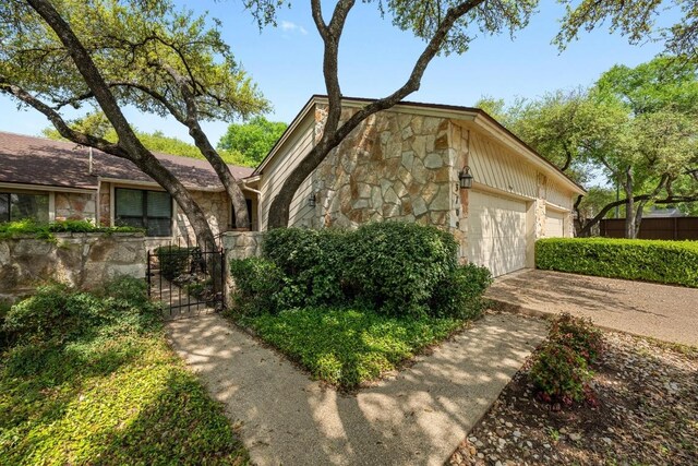 view of front of house with fence, an attached garage, concrete driveway, stone siding, and a gate