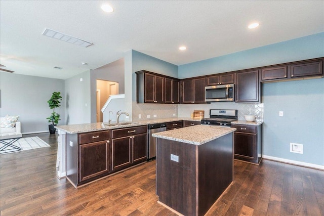 109 Pine Is, Leander, TX 78641 - kitchen with appliances with stainless steel finishes, dark brown cabinets, a peninsula, dark wood-style flooring, and light stone countertops