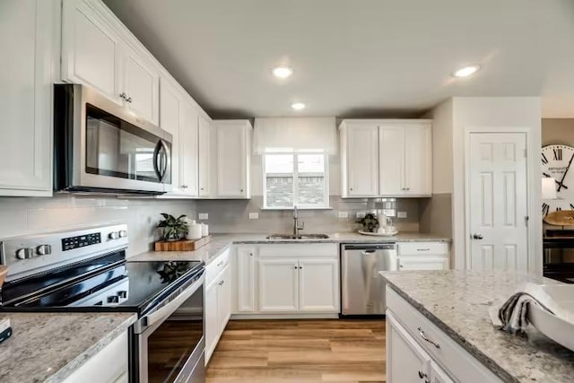 13328 Lapoynor St, Manor, TX 78653 - kitchen featuring stainless steel appliances, white cabinets, light wood-style floors, recessed lighting, and light stone counters