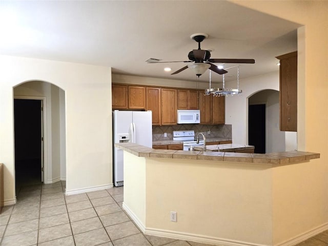 kitchen with white appliances, a ceiling fan, brown cabinetry, backsplash, and baseboards