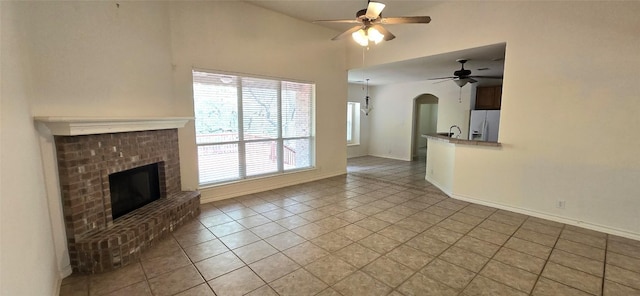 unfurnished living room featuring light tile patterned floors, a ceiling fan, arched walkways, a fireplace, and high vaulted ceiling