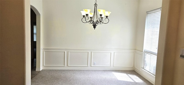 unfurnished dining area with arched walkways, a decorative wall, a chandelier, a wainscoted wall, and carpet flooring