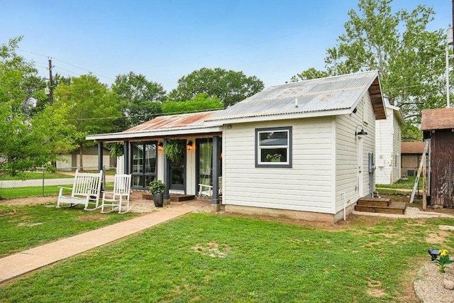 back of house with metal roof, fence, and a yard