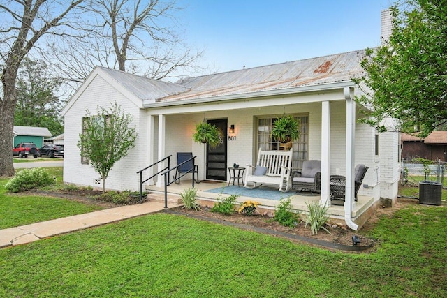 view of front of property with cooling unit, brick siding, a front lawn, metal roof, and a porch