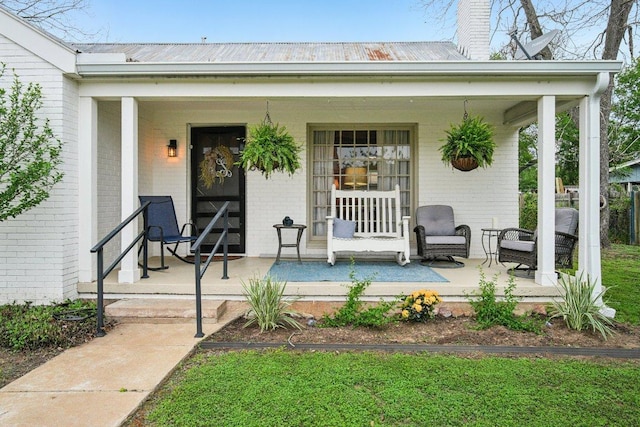 doorway to property with metal roof, covered porch, and brick siding