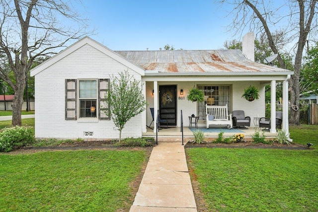 view of front of house featuring metal roof, a front yard, brick siding, a porch, and a chimney