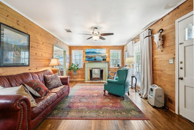 living room featuring hardwood / wood-style floors, wood walls, a fireplace, and ceiling fan