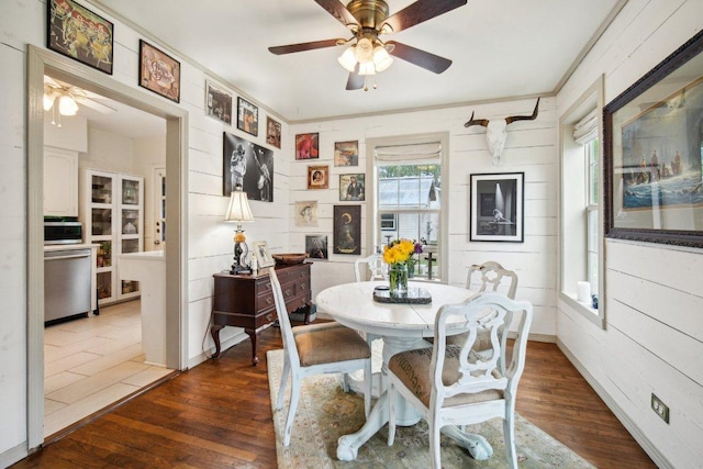 dining space featuring a ceiling fan, wooden walls, and wood finished floors