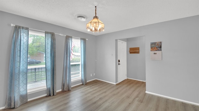 spare room with baseboards, a textured ceiling, wood finished floors, and a notable chandelier