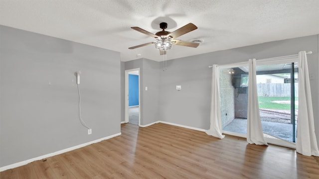 empty room with a textured ceiling, ceiling fan, baseboards, and light wood finished floors