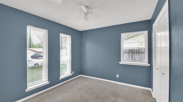 carpeted empty room featuring baseboards, a textured ceiling, and a ceiling fan