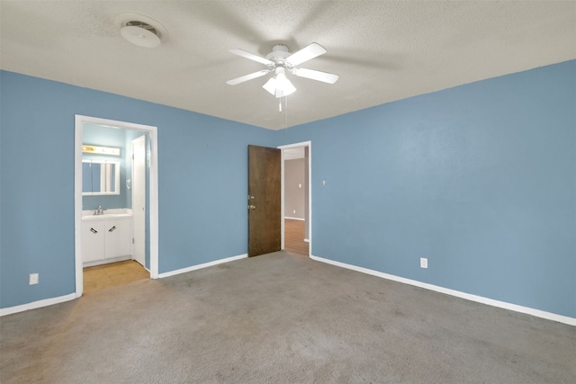 unfurnished bedroom featuring carpet flooring, baseboards, a textured ceiling, a sink, and a ceiling fan