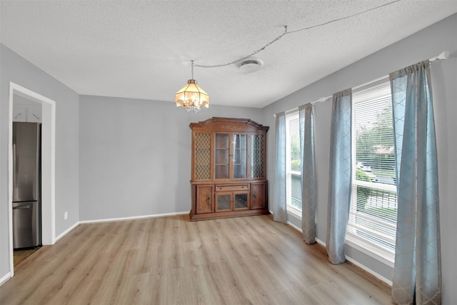 unfurnished dining area with baseboards, a textured ceiling, a notable chandelier, and light wood finished floors