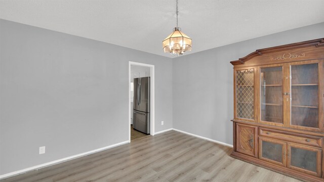 empty room with baseboards, wood finished floors, and an inviting chandelier