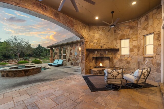 15086 Barrie Dr, Austin, TX 78734 - patio terrace at dusk with an outdoor stone fireplace, a ceiling fan, a patio, and an in-ground hot tub