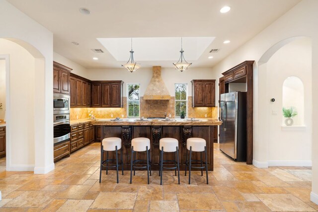 15086 Barrie Dr, Austin, TX 78734 - kitchen featuring appliances with stainless steel finishes, custom range hood, stone tile flooring, arched walkways, and recessed lighting