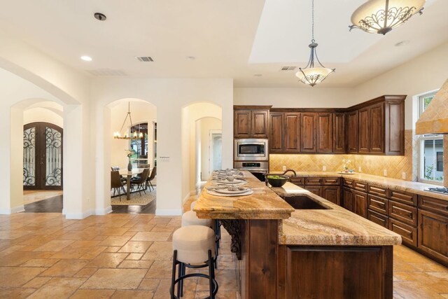 15086 Barrie Dr, Austin, TX 78734 - kitchen with appliances with stainless steel finishes, arched walkways, decorative backsplash, decorative light fixtures, and an island with sink