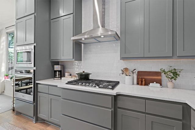 1213 Silver Dollar Trl, Georgetown, TX 78628 - kitchen featuring wall chimney exhaust hood, appliances with stainless steel finishes, gray cabinets, light wood-type flooring, and tasteful backsplash