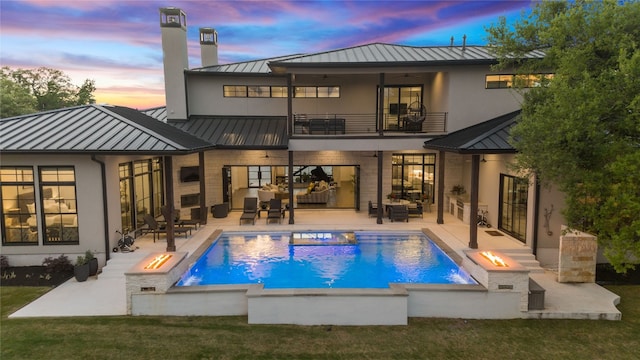 108 Fishspear Ln, Georgetown, TX 78628 - rear view of house with a standing seam roof, a balcony, metal roof, an outdoor living space with a fire pit, and a patio area