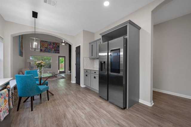 kitchen featuring light wood finished floors, stainless steel fridge with ice dispenser, arched walkways, and decorative backsplash