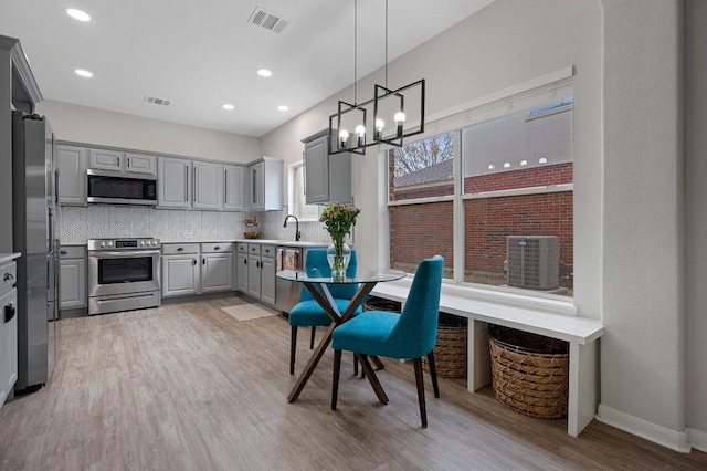kitchen with gray cabinetry, decorative backsplash, a sink, visible vents, and appliances with stainless steel finishes