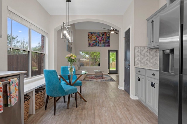 dining area featuring arched walkways, ceiling fan with notable chandelier, baseboards, and light wood-type flooring