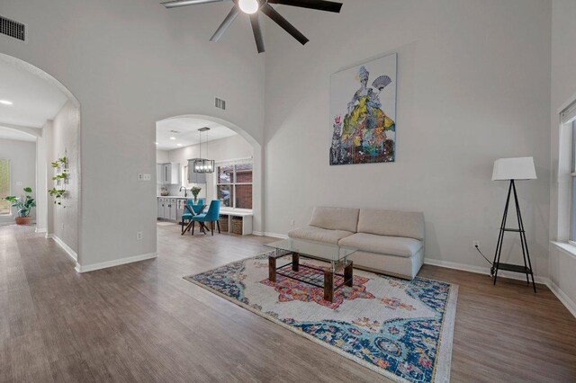 living area featuring arched walkways, ceiling fan, visible vents, and wood finished floors