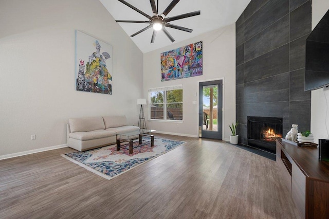 living area with high vaulted ceiling, baseboards, a fireplace, wood finished floors, and a ceiling fan