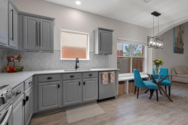 kitchen with gray cabinets, a chandelier, stainless steel dishwasher, a sink, and light wood finished floors