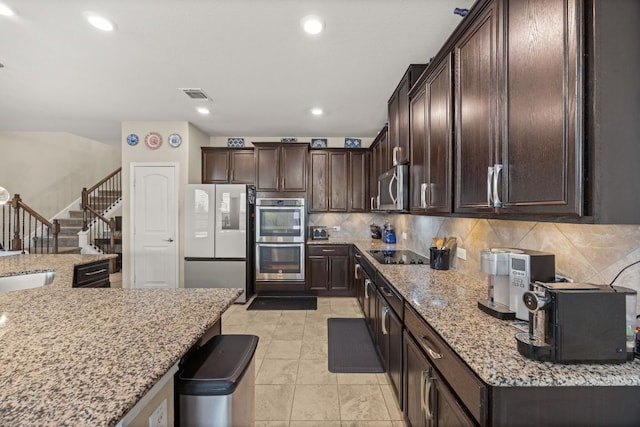 30336 Tiger Woods Dr, Georgetown, TX 78628 - kitchen featuring appliances with stainless steel finishes, dark brown cabinetry, decorative backsplash, light stone counters, and light tile patterned floors