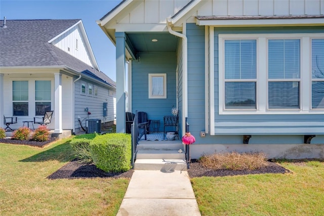 doorway to property with central AC unit, a lawn, covered porch, and board and batten siding