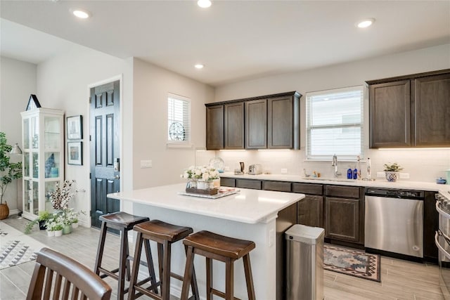 kitchen with dark brown cabinetry, backsplash, a sink, a kitchen breakfast bar, and stainless steel dishwasher