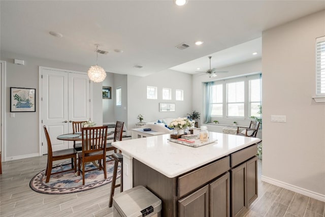 kitchen featuring wood finish floors, a ceiling fan, a kitchen island, and visible vents