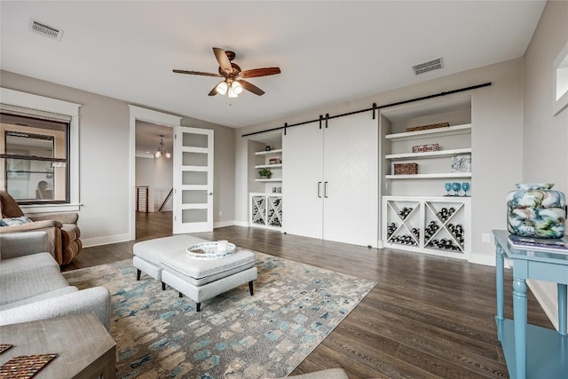 living room featuring a barn door, wood finished floors, visible vents, built in features, and ceiling fan