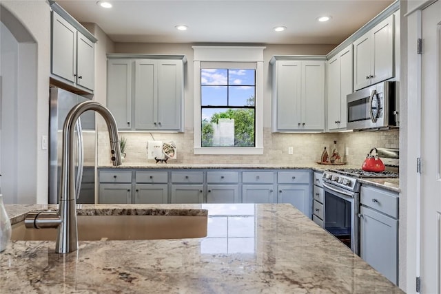 kitchen featuring arched walkways, recessed lighting, decorative backsplash, light stone counters, and appliances with stainless steel finishes