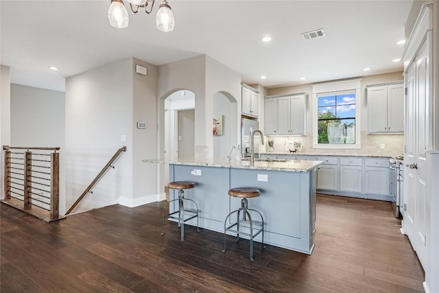 kitchen featuring light stone counters, a sink, a breakfast bar area, dark wood-type flooring, and visible vents