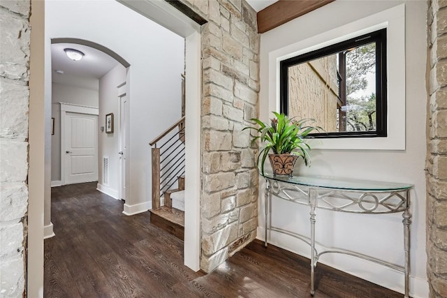 hallway featuring stairway, arched walkways, dark wood-style floors, and baseboards