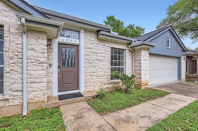 entrance to property featuring stone siding, driveway, and an attached garage