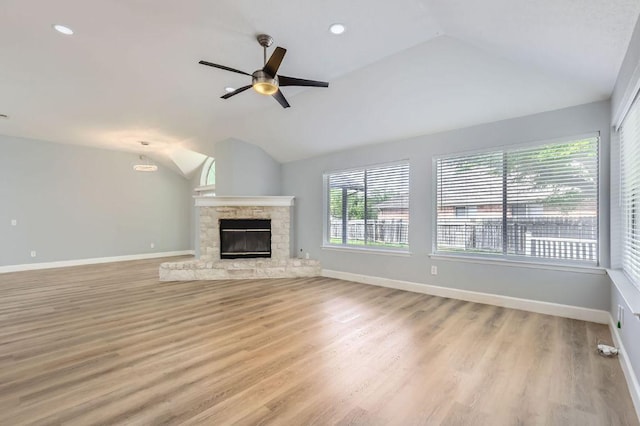unfurnished living room with baseboards, a stone fireplace, vaulted ceiling, and light wood finished floors