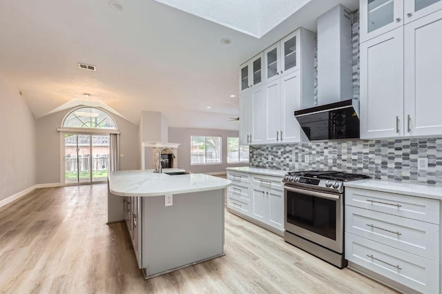 kitchen with a sink, wall chimney exhaust hood, lofted ceiling, stainless steel range with gas stovetop, and visible vents