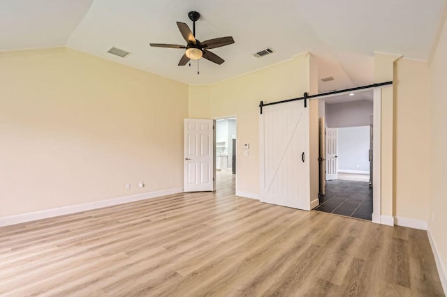 unfurnished bedroom with visible vents, a barn door, wood finished floors, and vaulted ceiling