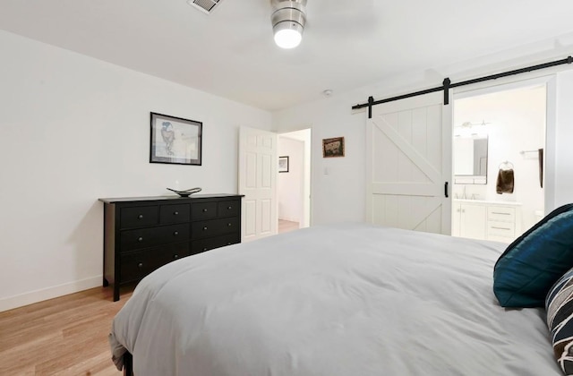 7511 Saint Cecelia St, Austin, TX 78757 - bedroom with a barn door, baseboards, light wood-style floors, and connected bathroom