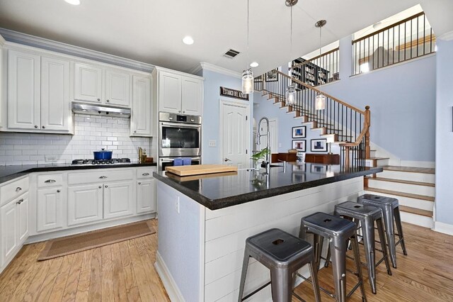 7721 Journeyville Dr, Austin, TX 78735 - kitchen with stainless steel double oven, light wood-type flooring, dark countertops, a kitchen breakfast bar, and white cabinetry