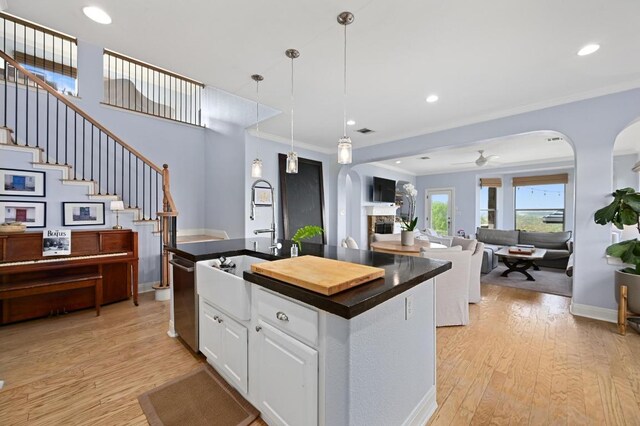 7721 Journeyville Dr, Austin, TX 78735 - kitchen with arched walkways, light wood finished floors, crown molding, a kitchen island with sink, and recessed lighting