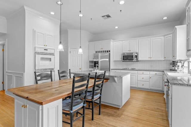 5305 Cuesta Verde, Austin, TX 78746 - kitchen with stainless steel appliances, a kitchen island, white cabinets, ornamental molding, and a kitchen bar