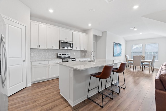 kitchen featuring light wood finished floors, decorative backsplash, a sink, and stainless steel appliances