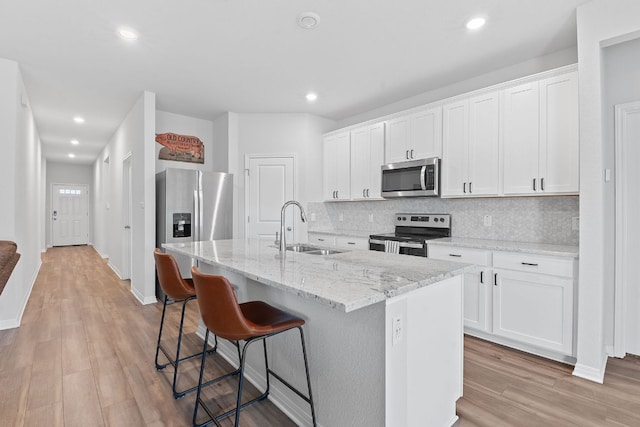 kitchen with decorative backsplash, a center island with sink, a sink, light wood-style flooring, and appliances with stainless steel finishes