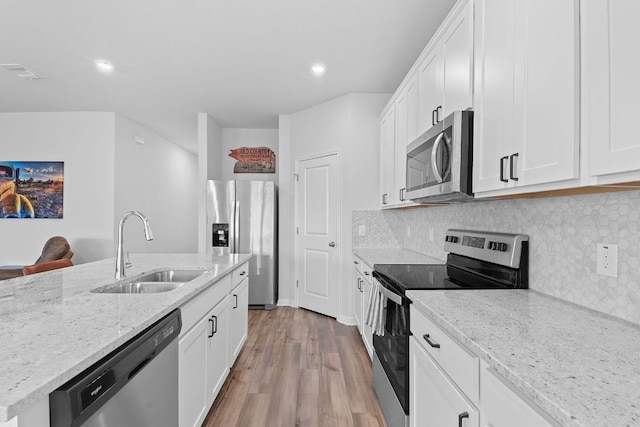 kitchen with light stone counters, a sink, light wood-style flooring, stainless steel appliances, and visible vents